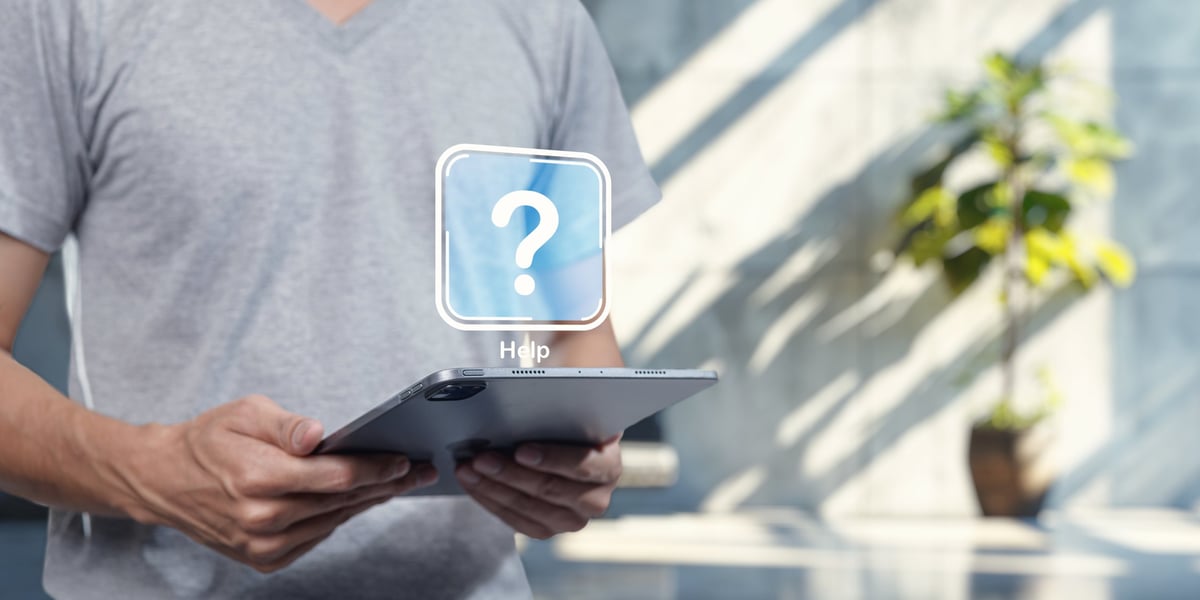 A person holds a tablet displaying a help icon, symbolizing software assistance. This image captures the essence of technology support, aiding users in navigating software programs effectively.